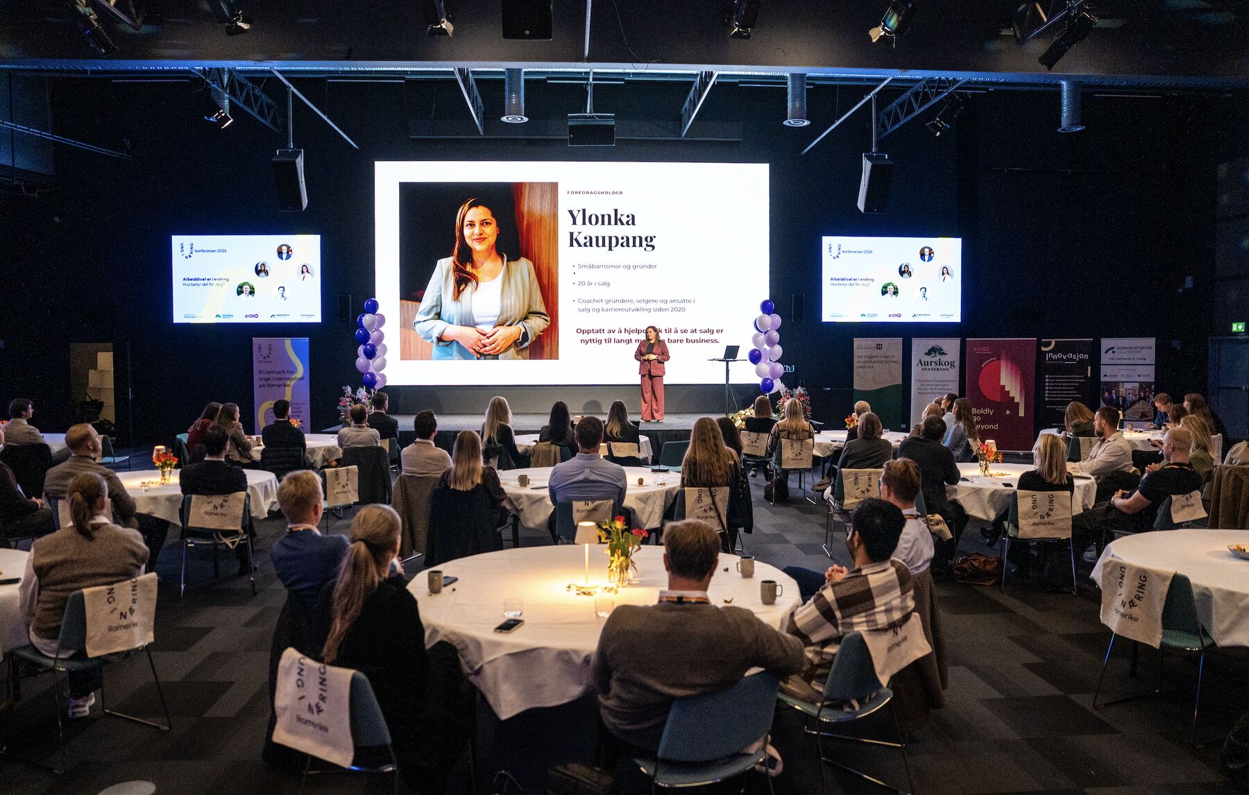 Ylonka Kaupang holder foredrag fra scenen for en fullsatt sal på Ung i Næring-konferansen